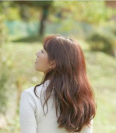 a woman with long red hair standing in the grass looking up to her left side