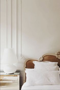 a bed with white sheets and pillows next to a lamp on a nightstand in a bedroom