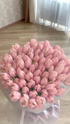 a bunch of pink tulips are in a vase on the floor next to a window