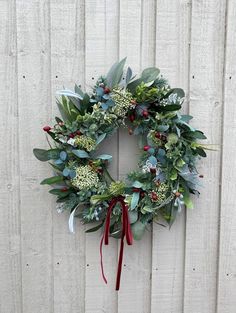 a wreath hanging on the side of a white fence with red ribbon and greenery