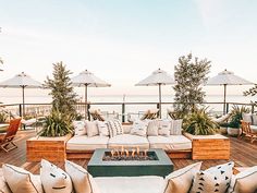 an outdoor living area with couches, tables and umbrellas over looking the ocean