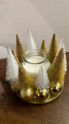 a glass jar filled with white and gold christmas trees sitting on top of a wooden table