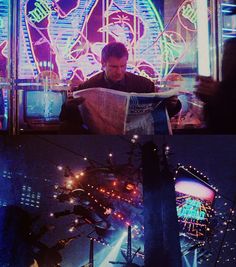 a man sitting at a table reading a newspaper in front of a carnival ride and ferris wheel