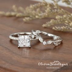 two engagement rings with leaves on them sitting on a wooden table next to some flowers