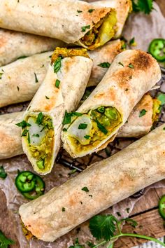 several burritos with green peppers and seasoning on a wooden table next to some cut up jalapenos