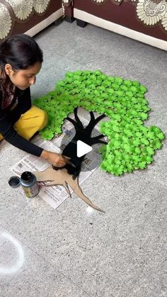 a woman sitting on the floor painting a tree with acrylic paint and glue