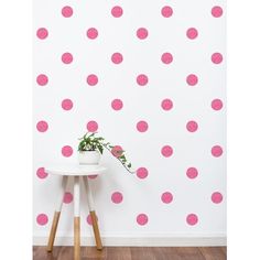 a pink polka dot wall decal on a white wall next to a small table with a potted plant