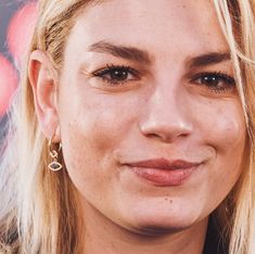 a close up of a woman with blonde hair and earrings on her neck smiling at the camera