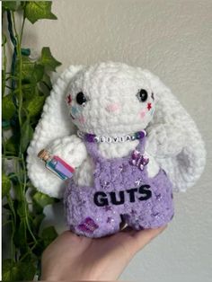 a hand holding a small stuffed animal with the word guts on it's chest