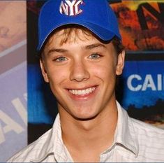 a young man wearing a new york mets cap and smiling at the camera while standing in front of a movie poster