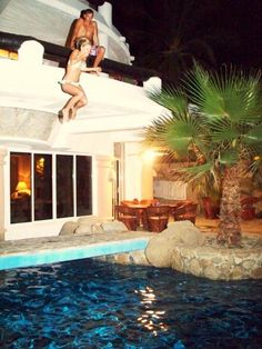 a man is jumping off the roof of a house into a swimming pool at night