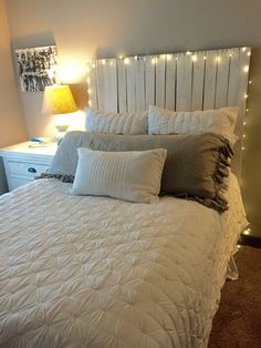 a white bed topped with lots of pillows next to a night stand filled with lights