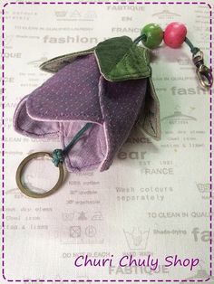 a keychain with a purple flower and green leaves on it, sitting on top of a table