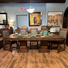 a dining room table set with blue dishes and place settings on it, in front of two framed pictures