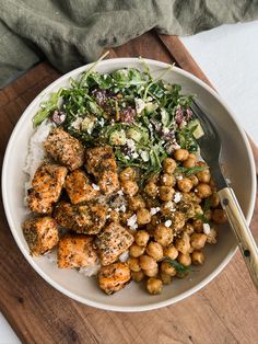 a white bowl filled with meat, rice and salad on top of a wooden cutting board