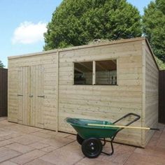 a green wheelbarrow in front of a wooden shed