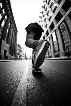 a person riding a skateboard down the middle of a street in front of tall buildings