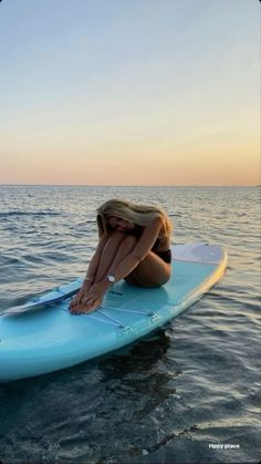 a woman sitting on top of a surfboard in the middle of the ocean at sunset