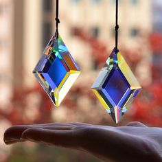 a person holding out their hand in front of a window with some colorful jewels hanging from it