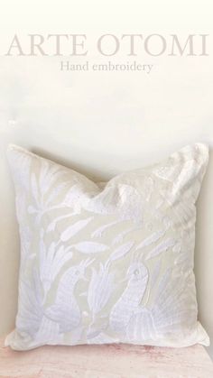 a white pillow sitting on top of a wooden table next to a wall with the words arte otomi hand embroidery