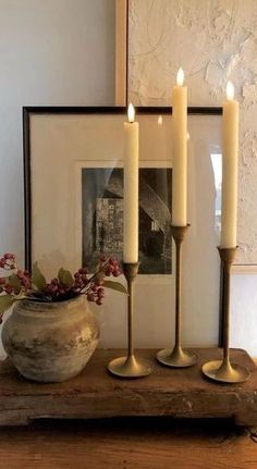 three candles sitting on top of a wooden table next to a vase with flowers in it