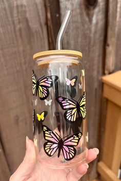 a person holding up a glass with butterflies painted on the side and a straw in their hand