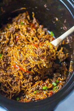 a slow cooker full of noodles and meat with a wooden spoon in the crock pot