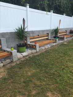 some wooden benches sitting in the grass near a white fence and planters with plants on them