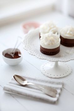 three small cakes on a white plate with spoons