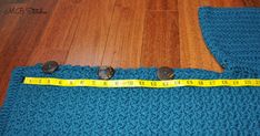 a blue crocheted sweater with buttons and measuring tape on the floor next to it