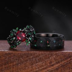 two rings sitting on top of a wooden table with green and red stones in them