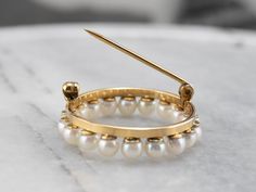 This vintage pearl circle brooch is a true classic! Simple and refined, traditional white pearls form a shimmering wreath, backed by rich yellow gold. This brooch would look wonderful pinned to a scarf or lapel, or even on a bridal bouquet! Love this piece but want to make it more versatile? We here at Market Square Jewelers, along with our master metalsmiths can convert this fantastic brooch into a necklace or pendant for an additional fee. Please contact us for more information! Metal: 10K Yel Elegant Yellow Gold Round Brooches, Timeless Wedding Brooch Jewelry, Classic Round Jewelry Brooch, Round Brooches With 17 Jewels For Wedding, Round Wedding Brooch With 17 Jewels, Classic Gold Round Brooches, Classic Yellow Gold Brooches For Wedding, Classic Yellow Gold Wedding Brooches, Classic Yellow Gold Round Brooches