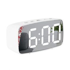 the alarm clock is white and has red numbers on it's face, with green leaves