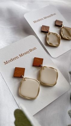 two pairs of earrings sitting on top of a white card next to some flowers and leaves