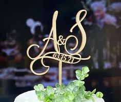 a wedding cake with the initials and name as well as green leaves on top is displayed in front of a black background