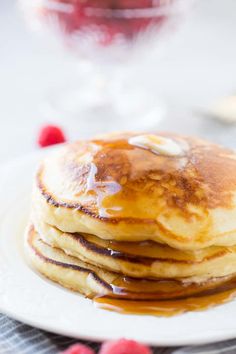 a stack of pancakes on a plate with syrup and raspberries in the background