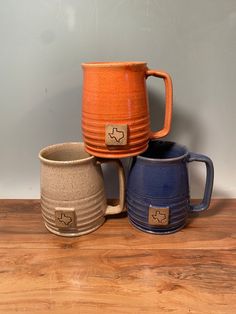 three different colored mugs sitting on top of a wooden table next to each other