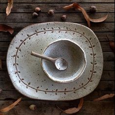 a white bowl with a spoon in it sitting on a wooden table surrounded by leaves and acorns