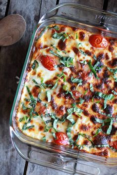 a casserole dish with tomatoes, cheese and herbs in it on a wooden table