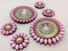 pink and gold brooches with pearls are arranged on a white table top next to each other