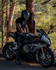 a man sitting on top of a black motorcycle in the middle of a wooded area