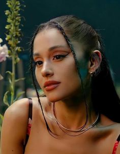 a young woman with braids on her head sitting in front of flowers and looking at the camera