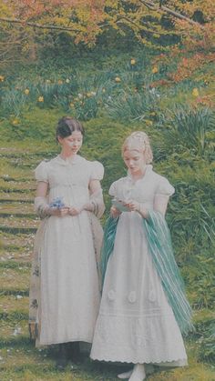 two women in white dresses standing next to each other on a grass covered field with flowers