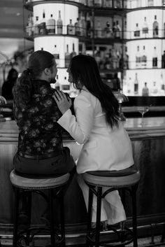 two women sitting at a bar with their backs to each other as they look into the distance