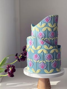 a blue and yellow cake sitting on top of a white plate next to a purple flower