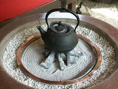 a tea pot sitting on top of a metal tray filled with rocks and gravel next to a red bench