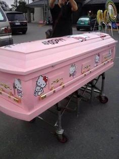 a pink hello kitty chest on wheels in a parking lot