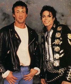 two people standing next to each other in front of a gray wall wearing black leather jackets