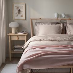 a bed with pink sheets and pillows on top of it next to a night stand