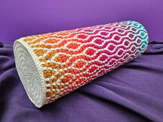 a multicolored crocheted pillow on a purple surface with a blue background